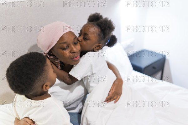 Two children hugging and kissing their sick mother in bed, showing support and love during cancer treatment