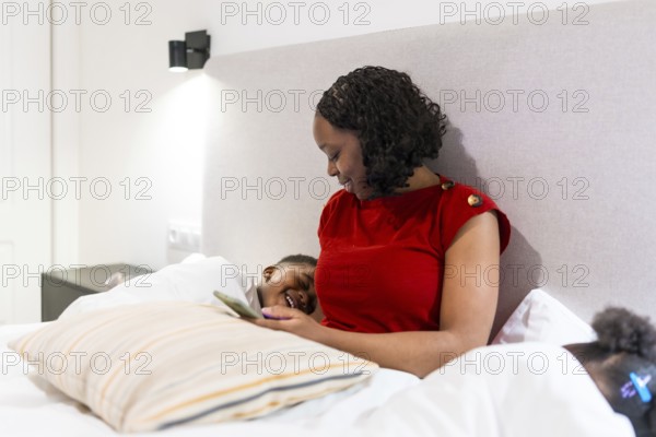 Smiling mother and son enjoying some quality time together while using a smartphone in bed