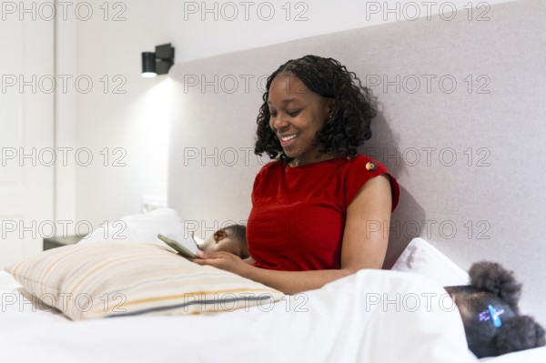 Smiling mother using her smartphone while two children sleep peacefully in bed, creating a serene and cozy atmosphere in the evening
