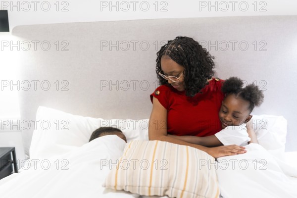 Young mother embracing her daughter in bed, while her son peacefully sleeping beside them, creating a warm and loving family moment
