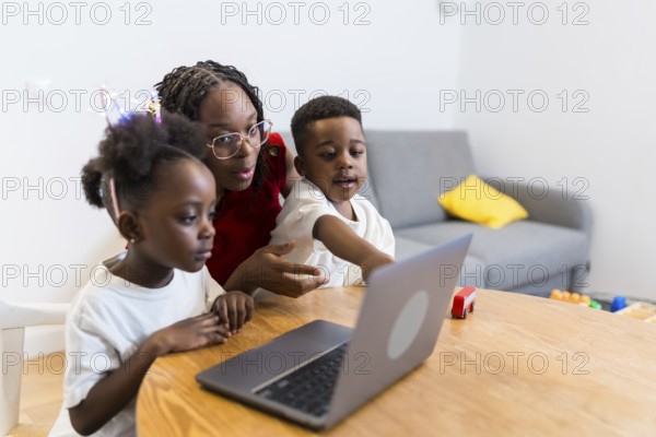 Young mother guiding her two children while using a laptop on a wooden table at home, fostering learning and connection in a cozy setting