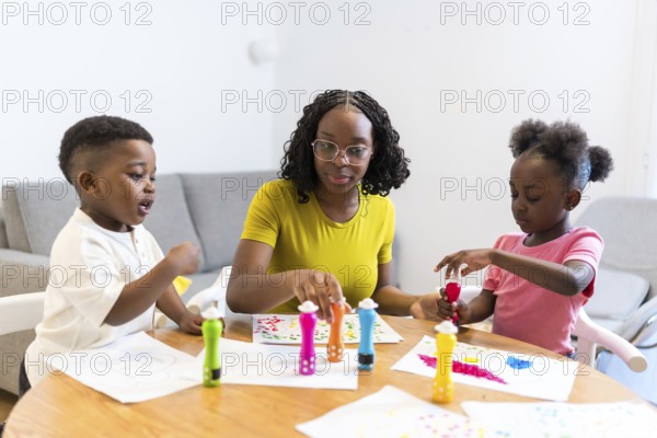 Mother and her two children enjoying creative time, painting colorful dots on paper at the dining table