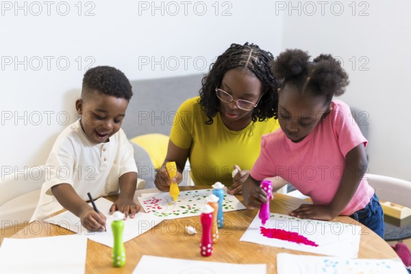 Mother and her two children are engaging in a creative painting activity at home, using colorful markers and enjoying quality family time together