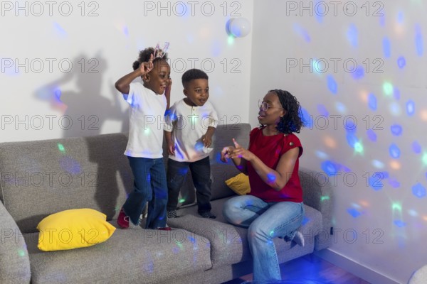 Mother and her two children enjoying dancing together in the living room, illuminated by colorful disco ball lights