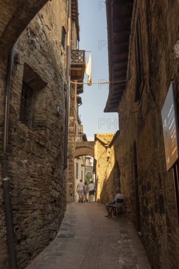 Alley in San Gimignano with historic walls, laundry in the wind and an elderly man on a chair, San Gimignano, Tuscany, Italy