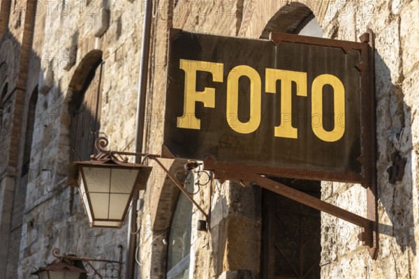 PHOTO sign in gold lettering hangs on a rustic stone wall in San Gimignano, Tuscany, Italy