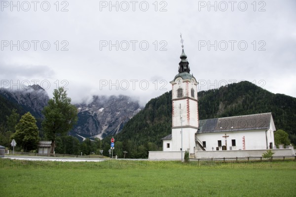 White church building against a mountainous background under a cloudy sky, Zgornje Jezersko, Gorenjska, Slovenia