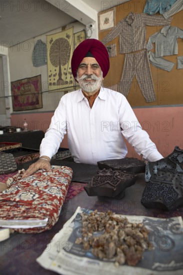 Indian Sikh, 68 years old, in his shop, in front bales of cloth and wooden panels for wood panel printing, Jaipur, Rajasthan, India