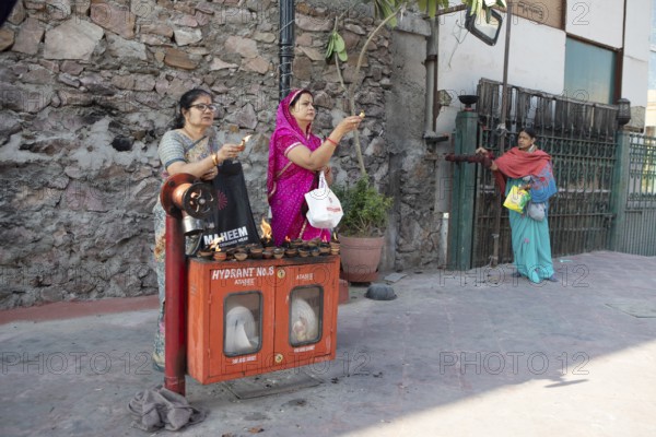 Indian woman holding tea lights in the air at a fire hydrant, Govind Dev Ji Hindu temple in the old city centre, Jaipur, Rajasthan, India