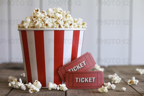 Red and white striped popcorn bucket with antique red movie tickets on rustic wooden table. Generative AI, AI generated
