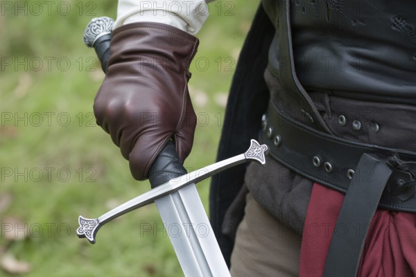 Close up of hand in leather glove holding medieval sword hilt with gemstone. Concept of medieval or LARP cosplay authenticity. Generative ai, AI generated