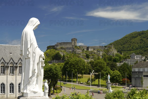 Statue on Rosary Square and the Château fort de Lourdes fortress in the Marian pilgrimage town of Lourdes, Pyrenees, France