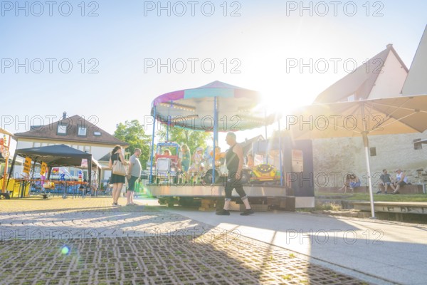 A carousel in the sunlight attracts cheerful people on a summer's day, 950 years of Weil der Stadt celebration, Böblingen district, Germany