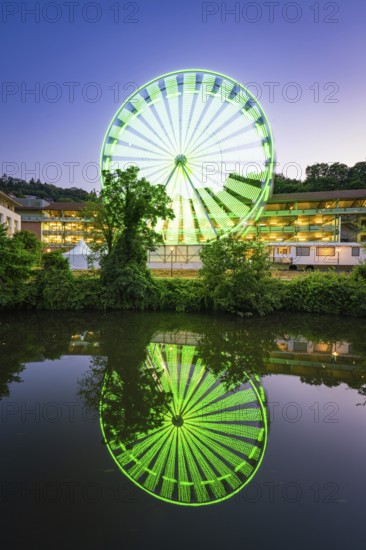 Green-blue illuminated Ferris wheel at night, reflected in the water, Calw, Germany