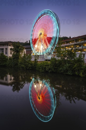 Illuminated Ferris wheel at night reflected in the water, in shades of blue and red, Calw, Germany