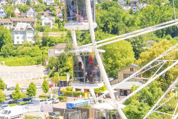 Detail of a Ferris wheel with passengers, surrounded by green trees and urban surroundings, Calw, Germany