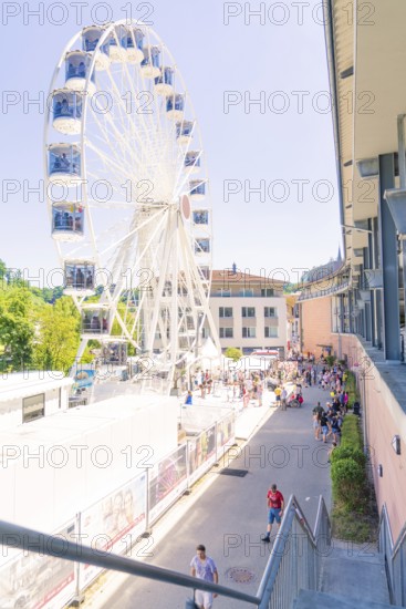 Ferris wheel next to a building with many people on a sunny promenade, Calw, Germany