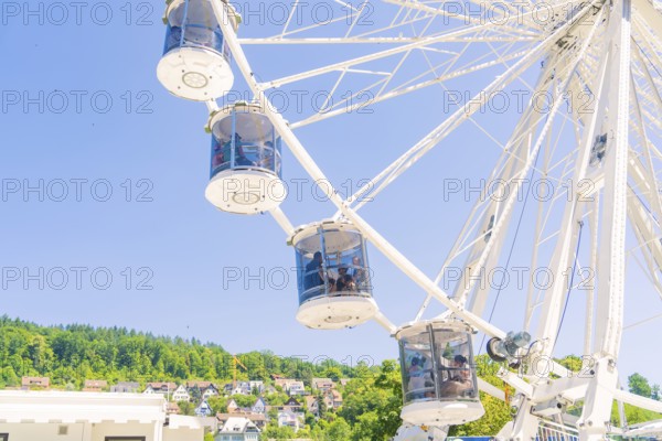 Ferris wheel with cabins in front of a blue sky, green trees and houses in the background, Calw, Germany