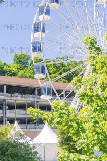 Close-up of the Ferris wheel, surrounded by green trees and tents against a blue sky, Calw, Germany