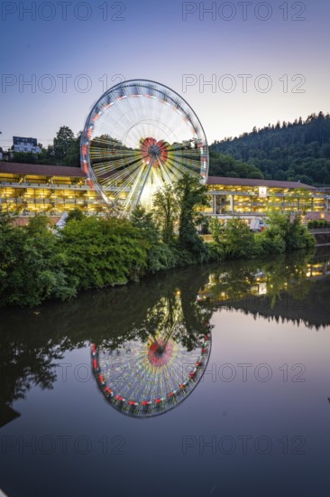 Illuminated Ferris wheel in a wooded landscape reflected in the water, Calw, Germany