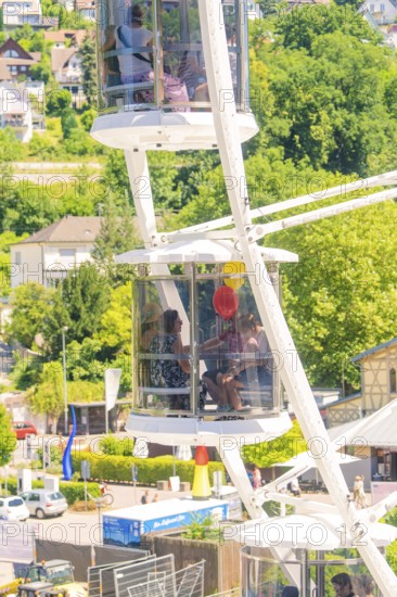 People in a Ferris wheel gondola with a view of green landscape and sunny weather, Calw, Germany