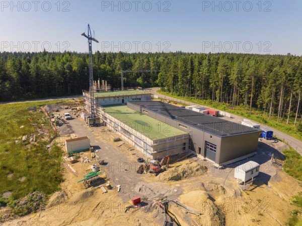 Outdoor construction site with solar roof and crane, surrounded by forest in sunny weather, new fire station, Oberhaugstett, district of Calw, Germany