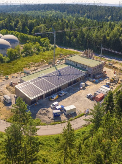 Aerial view of a construction site with solar panels and a crane, surrounded by dense forest and landscape, new fire station, Oberhaugstett, district of Calw, Germany