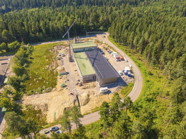 Solar roof building on a construction site surrounded by trees, crane and vehicles visible, aerial landscape perspective, new fire station, Oberhaugstett, district of Calw, Germany