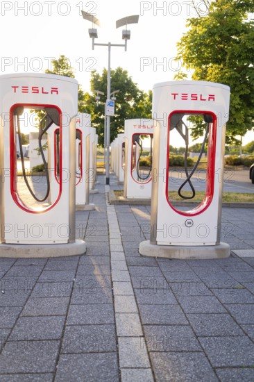 Several Tesla charging stations in an urban environment with sunlight and trees, Tesla Supercharger Böblingen, Germany