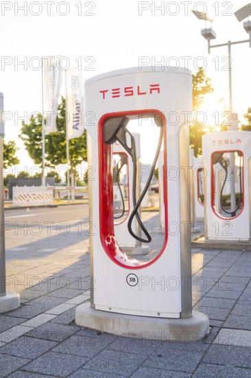 A Tesla charging station at sunset in an urban environment in front of green trees, Tesla Supercharger Böblingen, Germany