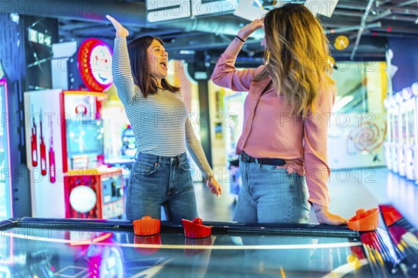 Two women giving high five while playing air hockey, enjoying their time together in entertainment venue