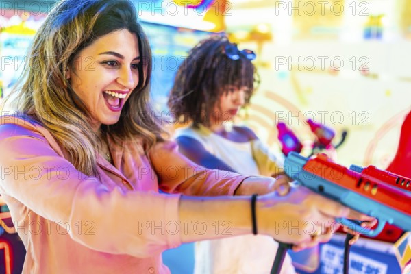 Two young women enjoying their summer vacation, playing arcade shooting games and having fun together