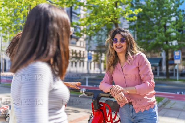 Group of friends talking and smiling next to a red electric scooter in a sunny summer day in the city