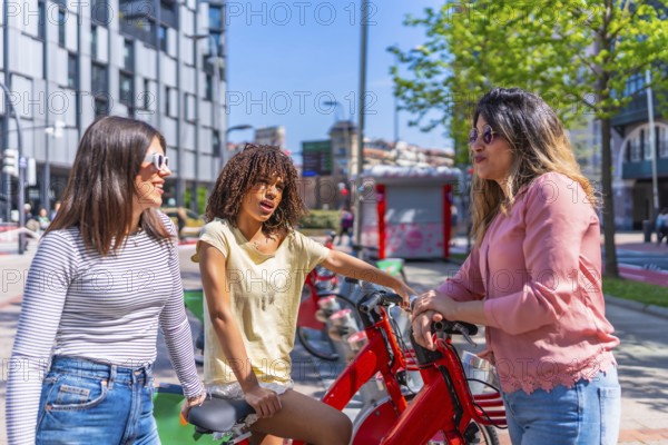 Three young women chatting happily near a bike sharing station in a vibrant city, enjoying a sunny day filled with laughter and friendship