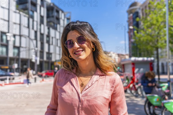Portrait of a beautiful brunette woman smiling wearing sunglasses in a city on a sunny summer day