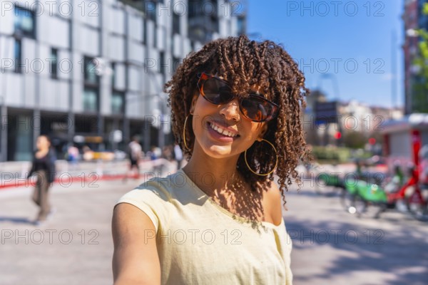 Smiling tourist enjoying a sunny day in the city, capturing the moment with a selfie while soaking up the vibrant urban atmosphere