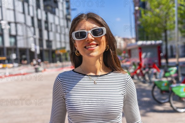 Portrait of a happy young woman wearing sunglasses and a striped shirt in a city center during a sunny summer day