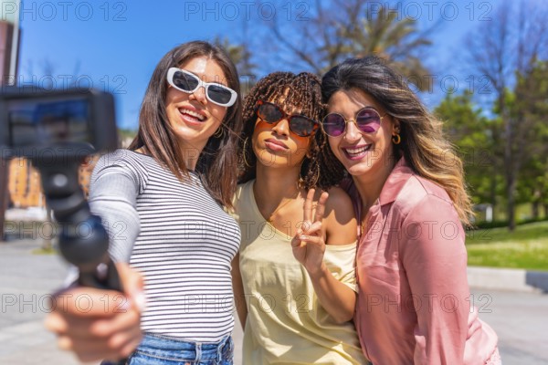 Three joyful women enjoying a sunny day, taking a selfie with an action camera while bonding during their summer vacation in the city park