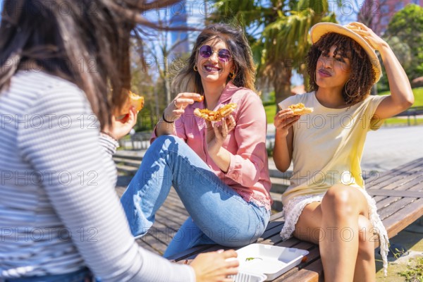 Young multi ethnic women having fun eating pizza slices in a park during a beautiful summer day