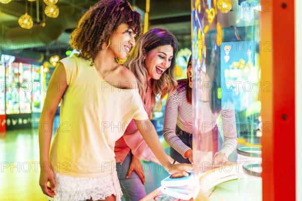 Three cheerful female friends enjoying their time together playing an arcade game in an amusement park