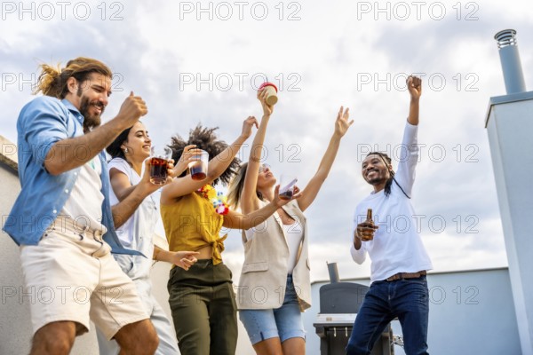 Cheerful multi ethnic friends dancing and enjoying drinks while having a fantastic time at a vibrant rooftop party under the city sky