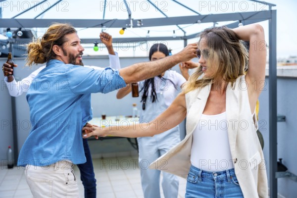 Cheerful young people dancing and having fun at a rooftop party, celebrating friendship and enjoying drinks