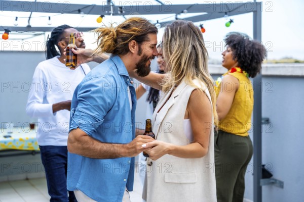 Happy couple dancing joyfully and sipping beer at a vibrant rooftop party, surrounded by diverse friends enjoying a lively summer evening