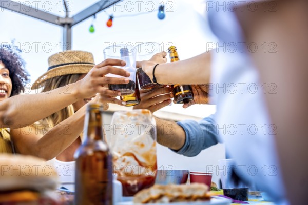 Diverse group of friends enjoying barbecue food and drinks, toasting together on a rooftop under string lights