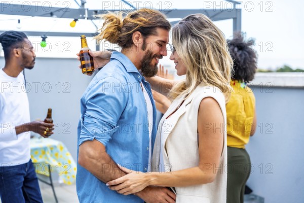 Happy couple embracing tenderly at a rooftop party, surrounded by friends enjoying drinks and good company