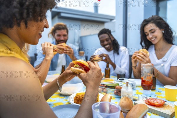 Cheerful multi ethnic friends savoring delicious burgers while enjoying a lively rooftop barbecue party filled with laughter and togetherness