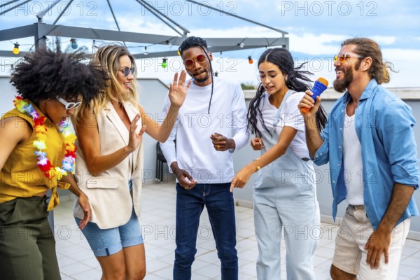 Group of cheerful multi ethnic friends having fun singing karaoke and dancing together at a rooftop party