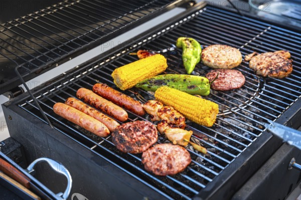 Sizzling sausages, juicy hamburger patties, tender chicken, and sweet corn cobs grilling over a barbecue, creating a mouthwatering feast