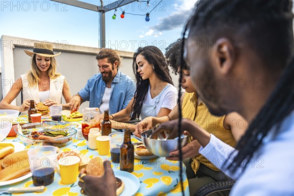 Multi ethnic friends enjoying a lively barbecue party on an urban rooftop, savoring delicious burgers and hot dogs while laughing together