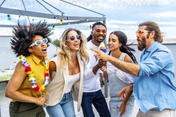 Cheerful multi ethnic friends enjoying a vibrant rooftop party, singing karaoke, dancing, and celebrating summer together under the city skyline